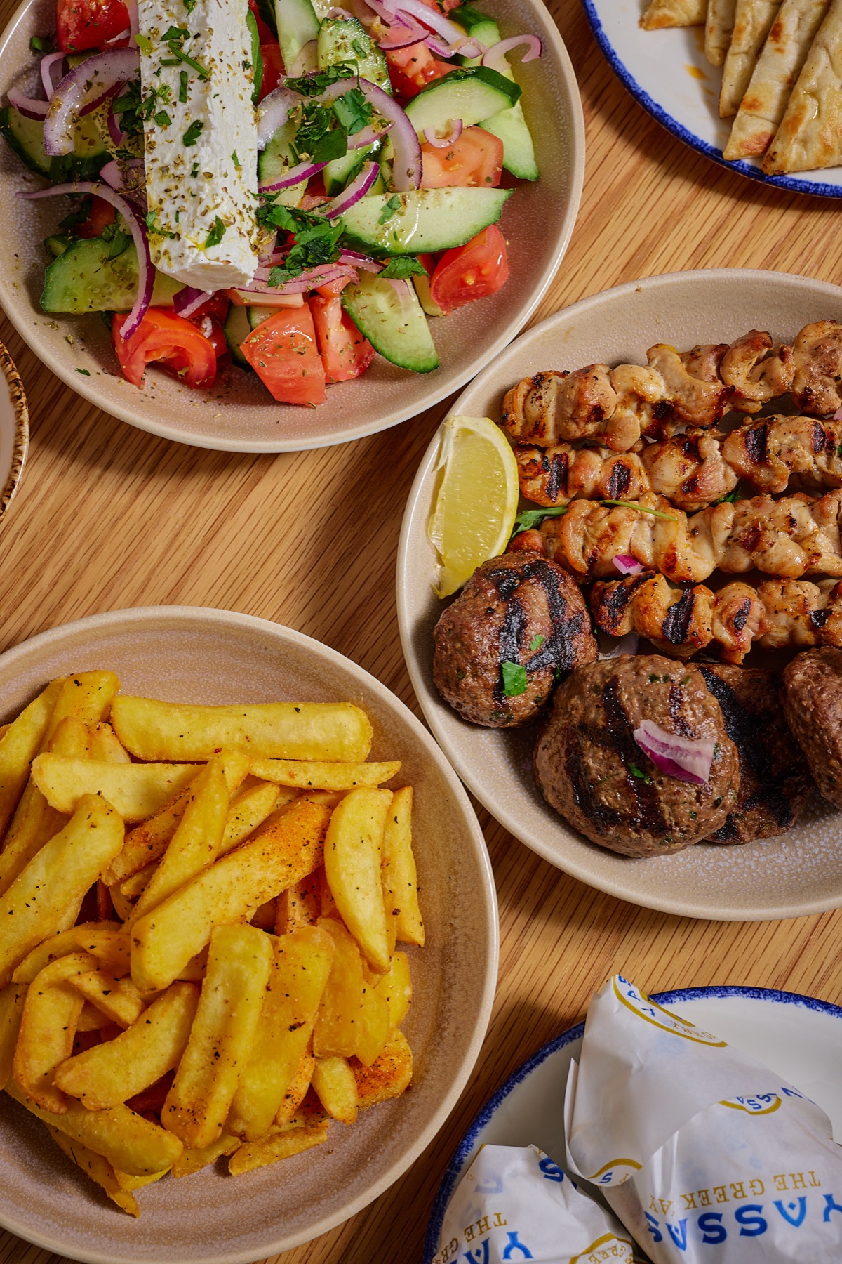 Close-up of chicken souvlaki skewers, kofta, Greek salad with feta, and hand-cut chips
